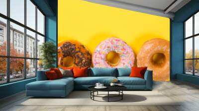 Three different donuts on yellow background. Top view and free space for text Wall mural