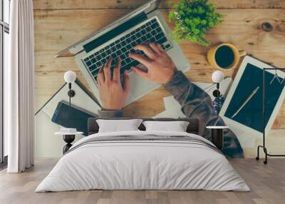 Businessman working on a laptop at office desk with paperwork and other objects around, top view Wall mural