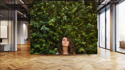 young woman smiling in the middle of a green wall full of plants and foliage Wall mural