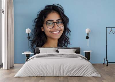 A beautiful Indian woman wearing glasses smiles and poses on light blue background. Wall mural