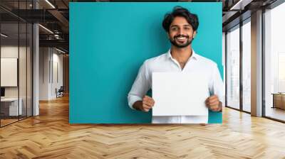 young indian man holding blank board on blue background Wall mural