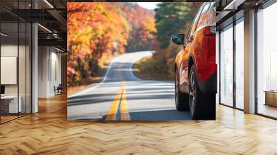 Red car drives down a winding road, flanked by vibrant autumn foliage under a clear sky, capturing the essence of a serene road trip. Wall mural