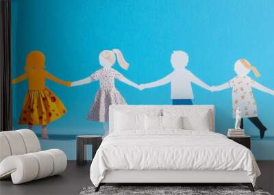 A cheerful collection of colorful paper cutout figures representing a diverse family holding hands in a circle under a bright yellow sun, symbolizing unity, love, and togetherness. Wall mural