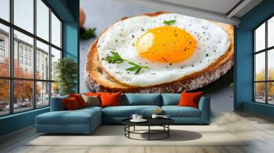 A close-up shot of a perfectly fried egg on toasted bread, seasoned with fresh herbs and black pepper. The yolk is runny and golden, inviting a delicious bite. The image symbolizes breakfast, comfort  Wall mural