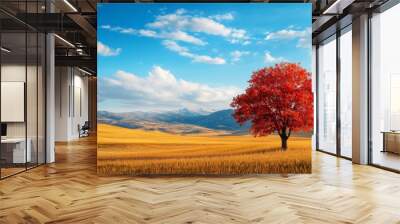 A lone red tree stands tall amidst a vast golden field, showcasing the vibrant colors of autumn. The blue sky with fluffy clouds creates a picturesque scene, symbolizing peace, serenity Wall mural