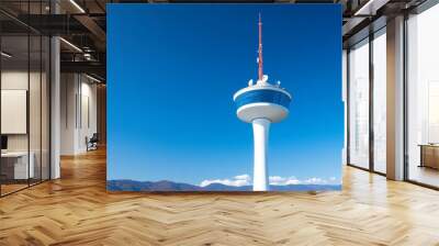 A white communications tower with a blue platform reaches towards a clear blue sky. The tower symbolizes connection, communication, progress, and technological advancement. Wall mural