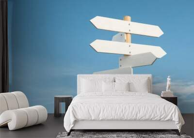 A white wooden signpost with multiple blank arrows pointing in different directions against a clear blue sky. This image symbolizes choice, opportunity, direction, and the potential for new beginnings Wall mural