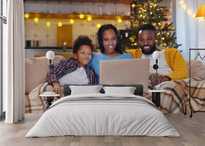 African-American couple and son sitting on couch having videocall with family on christmas eve Wall mural