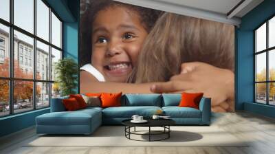 Back view of woman embracing funny african little girl isolated on blue background Wall mural