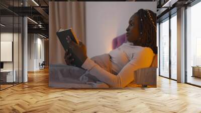 Beautiful young african woman reading book before going to sleep. Wall mural