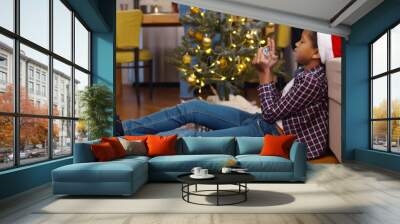 Lonely African-American child sitting on floor and playing on smartphone at christmas party Wall mural