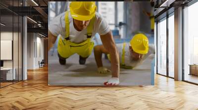 Mature builders in uniform doing pushups during break at work site Wall mural