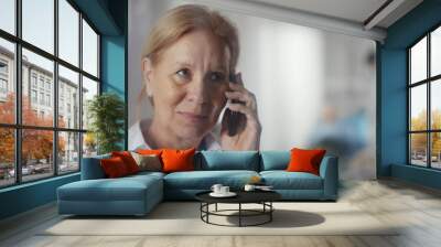 Mature female doctor standing near window and having phone call in hospital corridor Wall mural