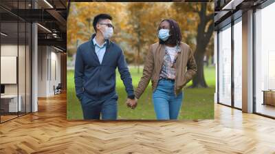 Multiethnic couple in protective masks holding hands walking in park Wall mural