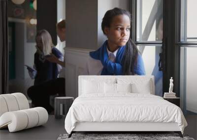 Portrait of sad African-American teen student sitting on window sill in corridor.  Wall mural