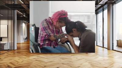 Portrait of sad young man kneeling before girlfriend in wheelchair at hospital Wall mural