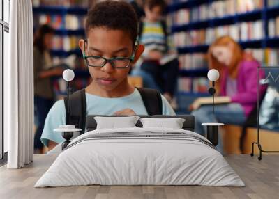 Smart african-american student boy reading book in library Wall mural