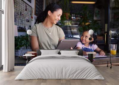 Black family, children and remote work in a coffee shop with a mother and daughter sitting together by a window. Kids, tablet and freelance business with a woman and female child bonding at a cafe Wall mural