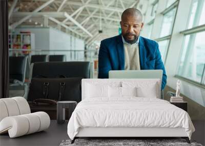 Black man, laptop and luggage at airport for business travel, trip or working while waiting to board plane. African American male at work on computer checking online schedule times for flight delay Wall mural