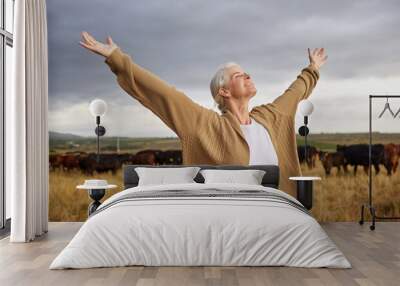 Happiness, freedom and mature woman looking free in nature with cows and grey sky background. Elderly happy senior relax with open arms in a countryside field with a smile and a positive mindset Wall mural