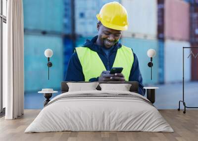 Social media, logistics and employee working in shipping typing on a mobile app with phone at a port. Happy African warehouse man reading an email or communication on a smartphone at industrial site Wall mural