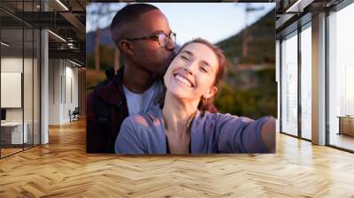 Interracial couple, kiss and smile for selfie, travel or love for adventure, journey or hiking together in nature. Happy man kissing woman smiling in happiness for photo moments, trip or traveling Wall mural