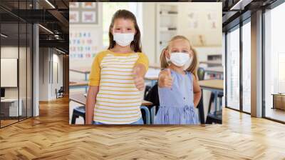 School kids, thumbs up and healthy students wearing masks in a classroom protecting against covid. Portrait of cute, young and friendly girls in a safe learning and educational environment together Wall mural