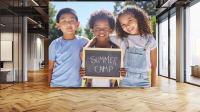 Summer camp, portrait or children with board in park together for fun, bonding or playing in outdoors. Sign, diversity or happy young best friends smiling or embracing on school holidays outside Wall mural