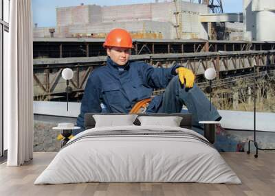 The worker rest on a construction site against on background of a large industrial enterprise. Wall mural