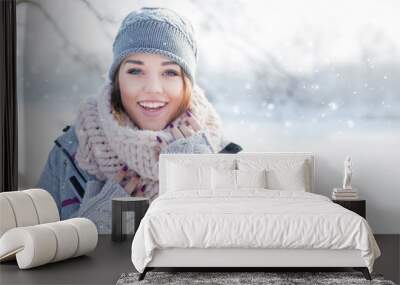 Beautiful  happy laughing young woman wearing winter hat gloves and scarf covered with snow flakes. Winter forest landscape background Wall mural