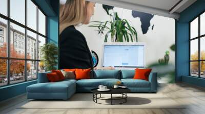 Happy businesswoman travel agent using laptop for communication and work on-line in modern environment with plants, booking flight. Travel agency arranging tour all over the world Wall mural