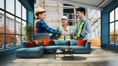 construction worker wearing a protective helmet and vest is holding his colleague's hand while working at the job site. Wall mural