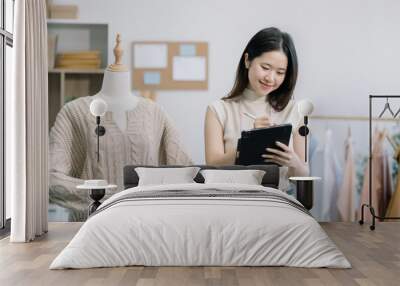 Female fashion designers design a product using a laptop computer with a digital tablet in a modern studio in the morning. Wall mural