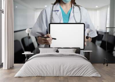 Front view of doctor woman standing holding tablet blank white screen at the office. Wall mural