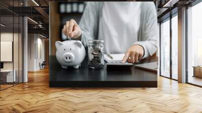 Woman sitting at desk managing expenses, calculating expenses, paying bills using laptop online, making household financial analysis, closer focus on the white piggy bank. Wall mural