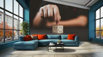 Man hand points on a wooden cube with happy smile face on bright side and unhappy face on dark side of wooden block cube for a positive mindset selection. Emotional state and mental health concept. Wall mural