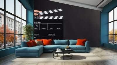 A hand is holding black clapper board or movie slate use in video production, movie, film, cinema industry on black background. It has written in number. Wall mural