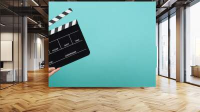 Hand is holding Black clapper board or clapperboard or movie slate on mint green or Turquoise background. Wall mural