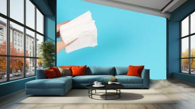 Hand is wiping and hold white paper tissue on blue background. Closeup. Empty space for text .Top down view. Wall mural