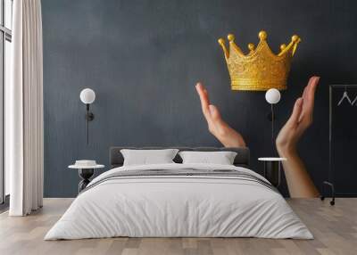 A golden crown is gently held between two outstretched hands against a dark background, symbolizing power, royalty, and achievement. Wall mural