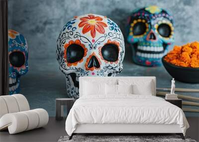 Colorful decorative skulls representing Dia de los Muertos, accented with bright flowers and paintbrushes, alongside a bowl of orange powder. Wall mural