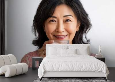 Mature Asian woman sipping from a glass of water, healthy aging concept, pure white backdrop, minimalistic Wall mural