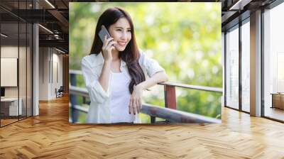 Beautiful young Asian businesswoman smiling while talking on her mobile phone with her customer outside the office	 Wall mural