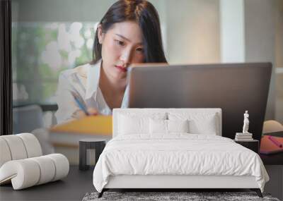 Young Asian woman using laptop computer and tablet PC to working in the modern co working space Wall mural