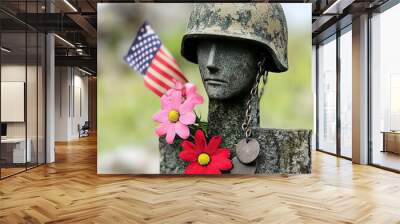 A weathered soldier's memorial with a helmet, adorned with flowers and an American flag, symbolizes honor and remembrance. Wall mural