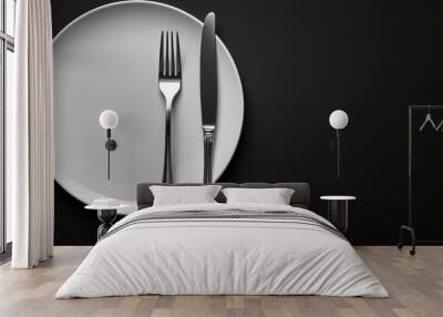 A white plate with a fork and knife on a black background Wall mural