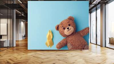 brown teddy bear holds in his paw a yellow ribbon folded in a loop on a blue background. concept of the fight against childhood cancer Wall mural