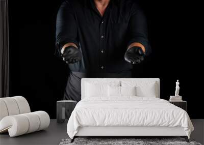 chef in a black shirt, apron and latex black gloves stands on a black background Wall mural