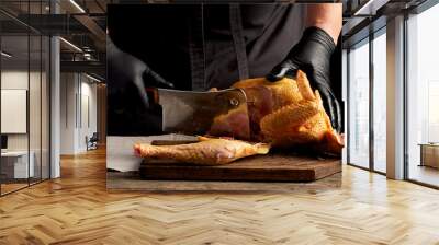 chef in black uniform and latex gloves chopping raw chicken into pieces Wall mural