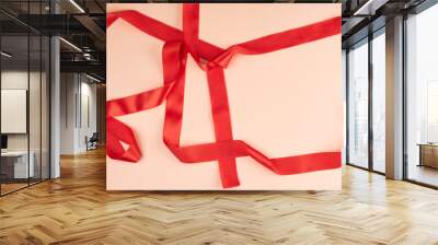 curled red satin ribbon on a beige background Wall mural